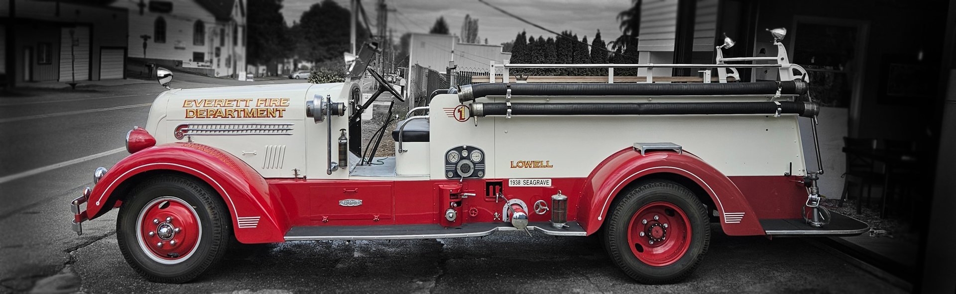 Vintage red and white fire truck parked on a residential street with early 20th century buildings in background