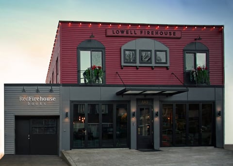 Modern red and gray firehouse building with storefront windows and signage for Lowell Firehouse and Red Firehouse