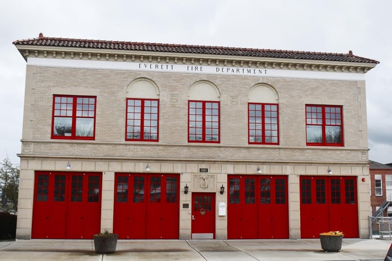 A brick fire station building with four large red garage doors on the ground level and five red-trimmed windows on the upper level